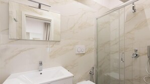 A bathroom with a white sink, a toilet, a glass shower enclosure, and a marble wall.