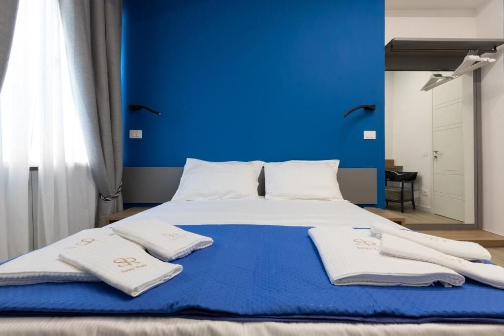 Een hotelkamer met een bed, blauwe wand, witte gordijnen en een spiegel.