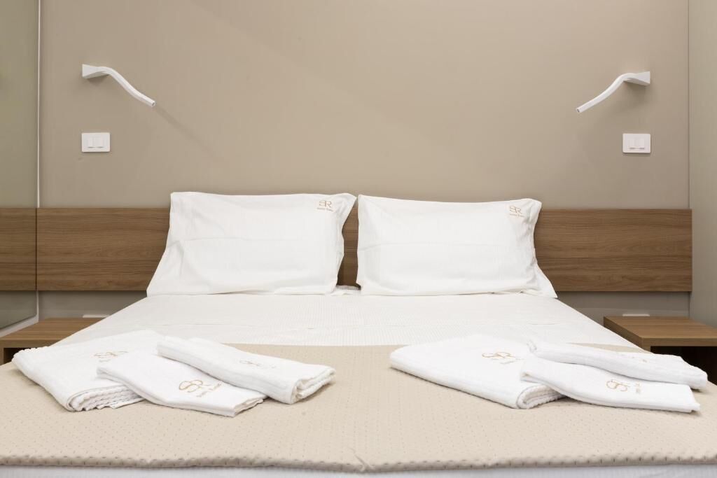 A neatly made bed with white linens and towels, a wooden headboard, and a wall-mounted light fixture.