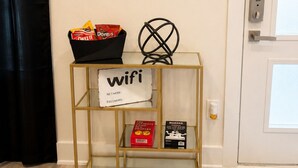 A room with a gold-framed console table holding a bag of Doritos, a sign indicating wifi availability, and a door with a keypad lock. - The Dallas Gem Tranquil 1-bedroom apartment with AC in vibrant Dallas (Dallas)