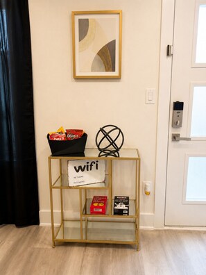 A room with a gold-framed console table holding a bag of Doritos, a sign indicating wifi availability, and a door with a keypad lock. - The Dallas Gem Tranquil 1-bedroom apartment with AC in vibrant Dallas (Dallas)