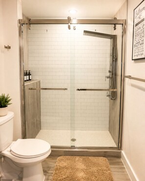 A bathroom with a glass-enclosed shower, a toilet, and a small rug. - The Dallas Gem Tranquil 1-bedroom apartment with AC in vibrant Dallas (Dallas)