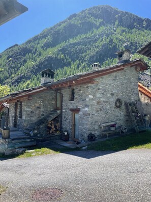 A stone building with a wooden staircase leading to a door, surrounded by a mountain backdrop. - Rifugio del Pettirosso (Martassina)