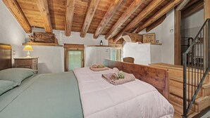 A bedroom with a wooden ceiling, a bed with a white duvet, a nightstand with a lamp, and a wooden headboard.