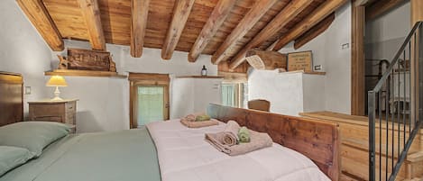 Une chambre avec un plafond en bois, un lit recouvert d’une couette blanche, une table de chevet avec une lampe et une tête de lit en bois.