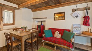 A cozy room with a wooden ceiling, a red plaid sofa, a wooden dining table with chairs, and a small red heater.