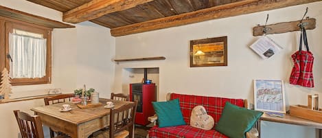 A cozy room with a wooden ceiling, a red plaid sofa, a wooden dining table with chairs, and a small red heater.