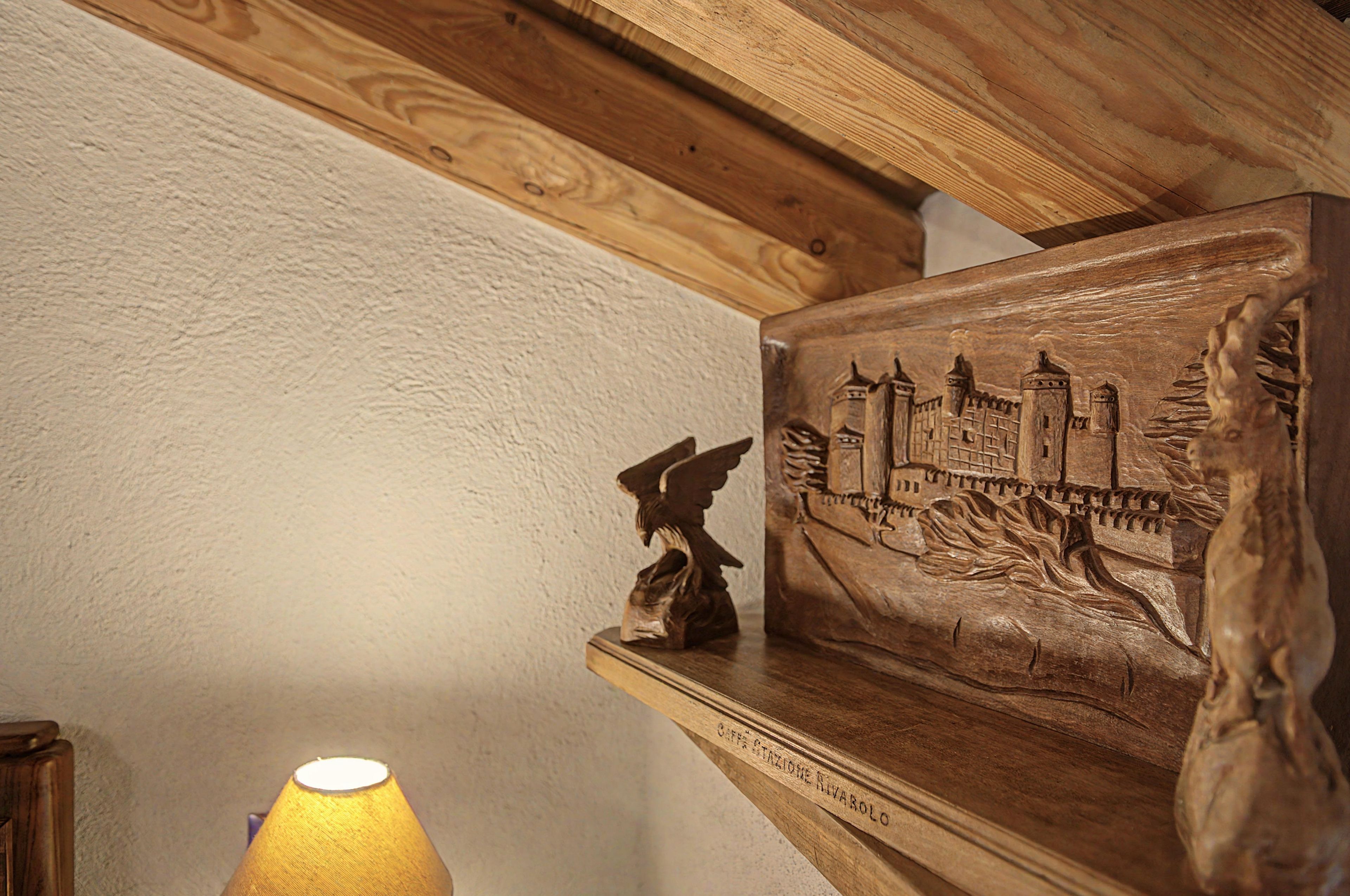 A wooden shelf with a carved relief of a castle and a winged figure, placed against a textured wall.