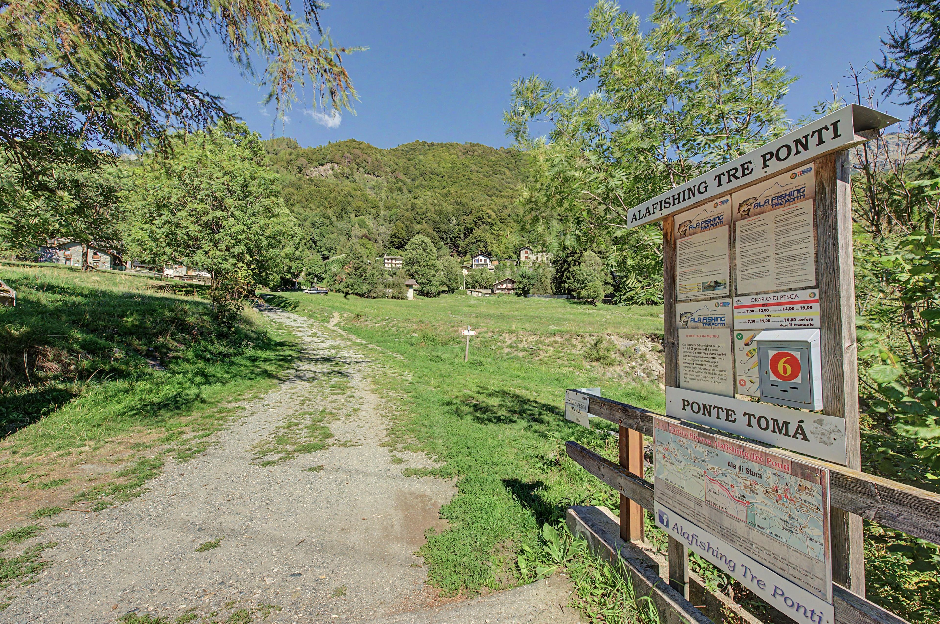 Ein Wegweiser mit Informationen über alafishing tre ponto, ein Pfad, der durch eine grüne Landschaft führt, und ein Holzzaun.