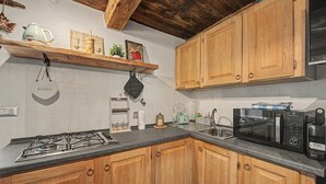Une cuisine avec des meubles de rangement en bois, une cuisinière à gaz, un four à micro-ondes et une étagère contenant des ustensiles de cuisine.
