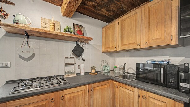 A kitchen with wooden cabinets, a gas stove, a microwave, and a shelf with kitchen items.