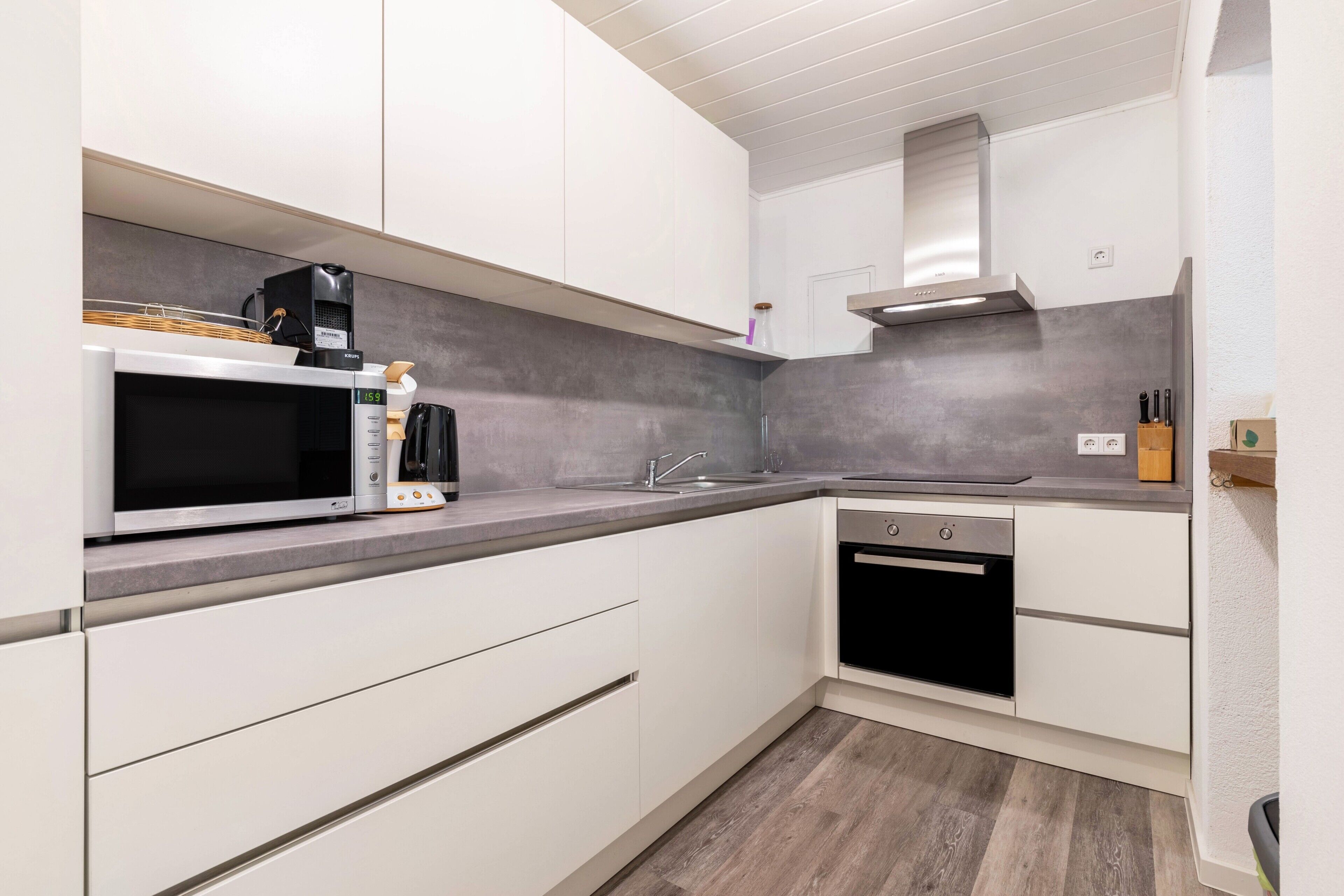 A modern kitchen with white cabinetry, a microwave, a coffee maker, a sink, and an oven.