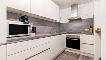 A modern kitchen with white cabinetry, a microwave, a coffee maker, a sink, and an oven.