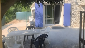 Un patio exterior con una mesa y sillas, un muro de piedra y un área cubierta con una puerta corrediza.