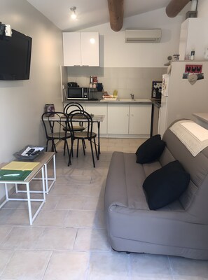Ein kompakter Wohnbereich mit Sofa, Esstisch und Stühlen, einer kleinen Küchenzeile mit Mikrowelle und einer Klimaanlage.