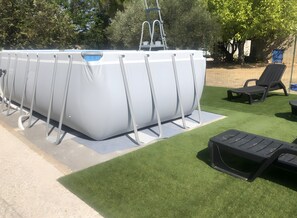 Ein Swimmingpool mit einer Leiter, umgeben von Rasenteppich und zwei Liegestühlen.