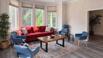 Uma sala de estar moderna com um sofá vermelho, cadeiras azuis, uma mesa de centro de madeira e grandes janelas com persianas.