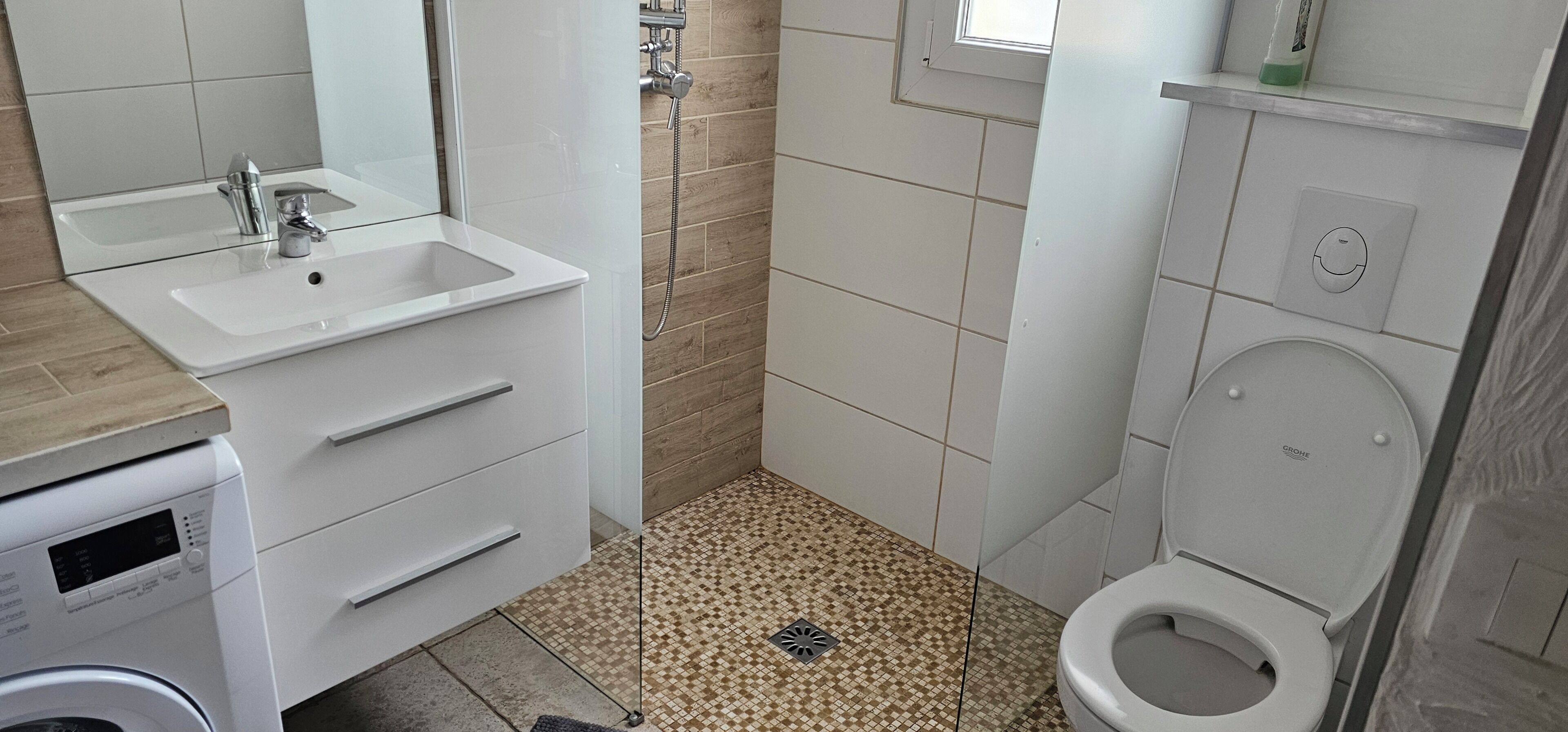 Une salle de bain équipée d’un lavabo, d’un miroir, d’une douche, de toilettes et d’un lave-linge.
