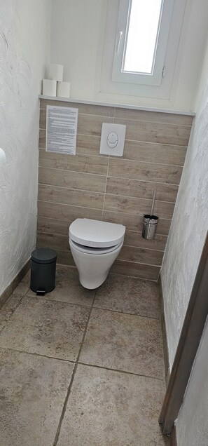 Ein kleines Badezimmer mit Toilette, Mülleimer und Fenster.
