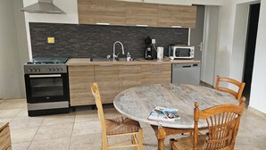 Ett modernt kök med en spis, mikrovågsugn och diskho. Där finns ett runt träbord med stolar och en tidning ligger på bordet.