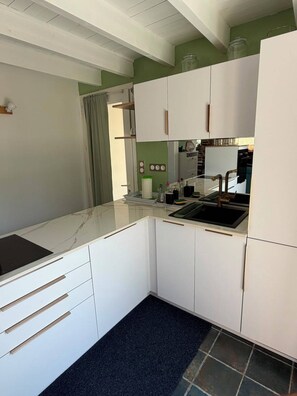 A compact kitchen with white cabinetry, a black countertop, and a tiled backsplash. - Vacation Rental in the Brocéliande Forest (Néant-sur-Yvel)