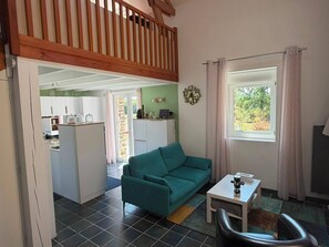 A living area with a teal sofa, a small table, and a window with curtains. - Vacation Rental in the Brocéliande Forest (Néant-sur-Yvel)