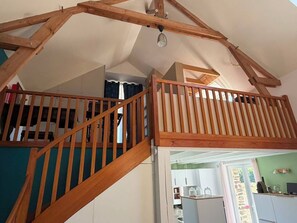 A loft-style room with exposed wooden beams, a staircase, and a view into a kitchen area. - Vacation Rental in the Brocéliande Forest (Néant-sur-Yvel)