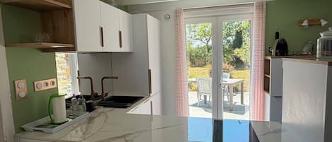 Una cocina moderna con armarios blancos, encimera de mármol y puerta corredera de vidrio que da a un patio exterior.