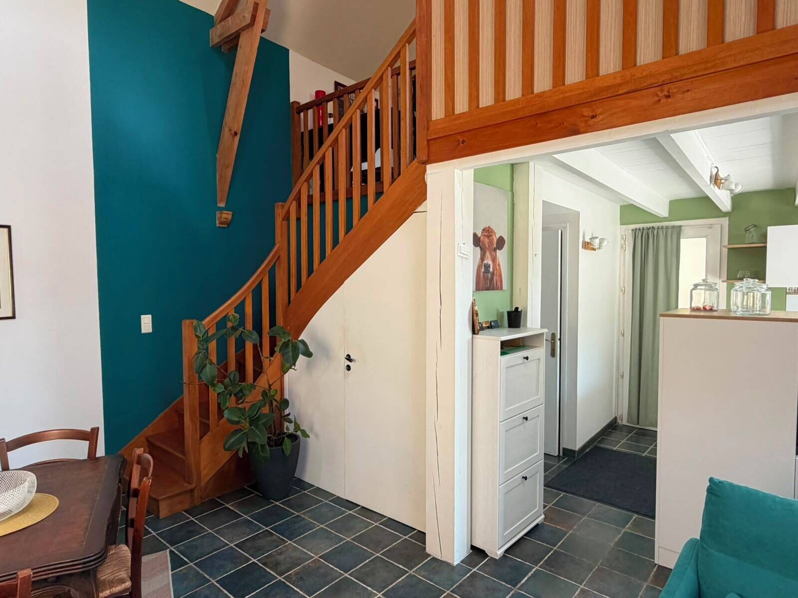 A staircase with wooden railings leading to a room with a green wall, a white cabinet, and a dining area with a table and chairs.