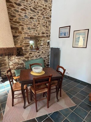 A dining area with a stone wall, a table with chairs, and two framed pictures on the wall. - Vacation Rental in the Brocéliande Forest (Néant-sur-Yvel)