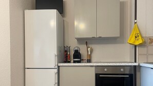 Une cuisine compacte équipée d’un réfrigérateur, d’un four et d’une machine à café posée sur le plan de travail.