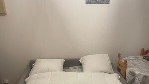 Un lit avec une literie blanche, une tête de lit en bois et une petite table recouverte d’une nappe à motifs.