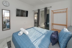 Ein Schlafzimmer mit Bett, Fernseher, Fenster mit Vorhängen und einem Holzregal.