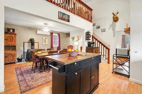 A spacious kitchen with a central island, wooden flooring, a staircase, and a mounted deer head.