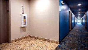 Corridoio di un hotel con un rilevatore di fumo sulla parete, pavimento rivestito di moquette e porte su entrambi i lati.