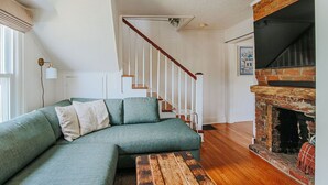 A green sofa, wooden bench, staircase, and brick fireplace in a living room. - The Mariposa (Staunton)