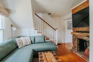A green sofa, wooden bench, staircase, and brick fireplace in a living room. - The Mariposa (Staunton)