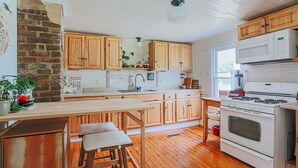 A kitchen with wooden cabinets, a white stove, and a wooden bar stool. - The Mariposa (Staunton)