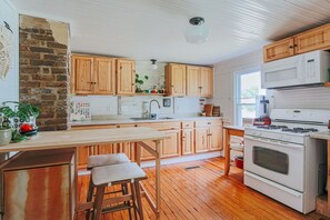A kitchen with wooden cabinets, a white stove, and a wooden bar stool. - The Mariposa (Staunton)