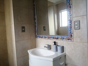 A bathroom with a white sink, a large mirror with a decorative border, and a window. - Oceana Suites Hacienda Limache (Limache)