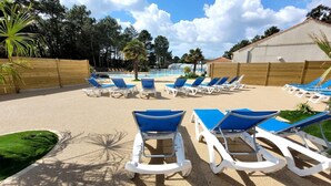 Un espace aménagé au bord de la piscine, avec des chaises longues, une piscine et un bâtiment doté d’un toit en tuiles.