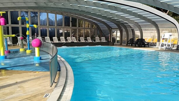 Une piscine intérieure dotée d’un toit incurvé, d’une eau cristalline et d’un espace de jeux avec des équipements colorés.