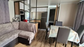 Un espace de vie compact comprenant un canapé, une table à manger avec des chaises, un coin cuisine et une porte coulissante donnant sur une autre pièce.