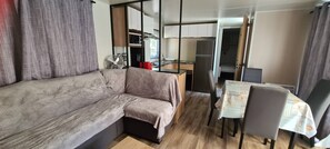 Ein kompakter Wohnbereich mit Sofa, Esstisch mit Stühlen, einer Küchenzeile und einer Schiebetür zu einem weiteren Raum.