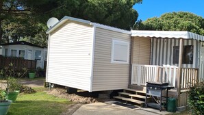 Une maison mobile avec une véranda, un barbecue et une antenne parabolique.