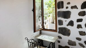 Ein Zimmer mit Steinwand, einem Fenster, einem Tisch mit Stuhl und einem Bett.