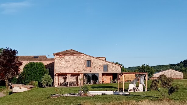 Un bâtiment en pierre avec un toit en tuiles, un patio couvert avec des meubles d’extérieur et une cour gazonnée.