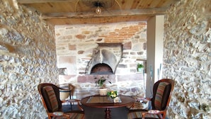 Une pièce aux murs de pierre, avec une table ronde en bois et deux chaises, une cheminée en briques et un luminaire suspendu.