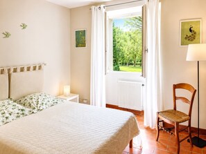 A bedroom with a bed, a chair, a nightstand, a lamp, a window with curtains, and a radiator. - Welcome to the Serrepile large holiday home,large swimming pool and tennis court (Lempaut)