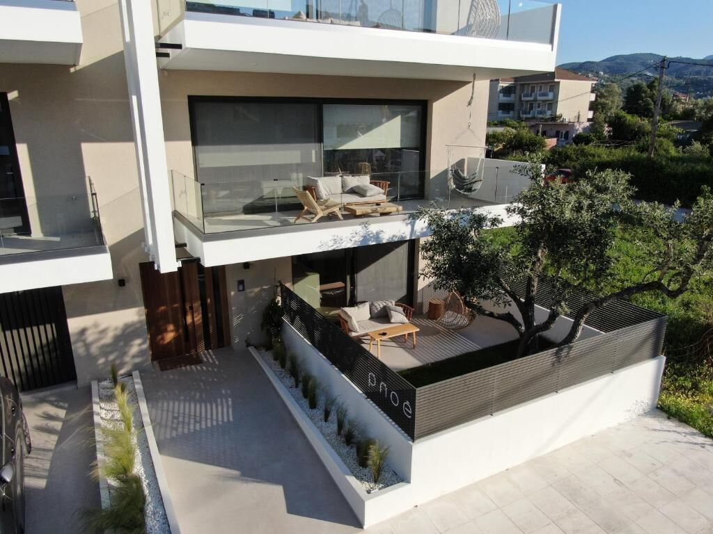 Una casa moderna de dos pisos con balcón, mobiliario exterior y un jardín.